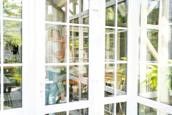 Liebespaar küsst und umarmt sich in der Küche. Blick vom Garten — Stockfoto