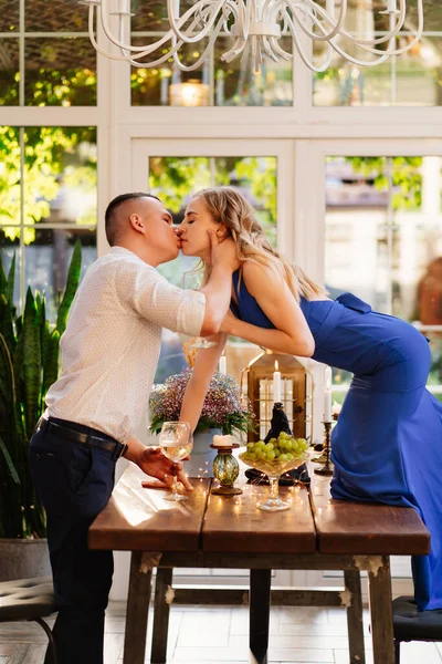 Romantik yemek. Bir bardak şarabı olan kız, erkek arkadaşını öpmek için masanın üzerinde duruyor..