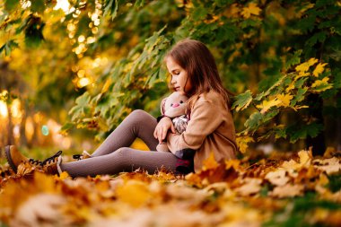 Düşen yaprakların üzerinde oturan üzgün küçük kız. Çocukların kırgınlığı.