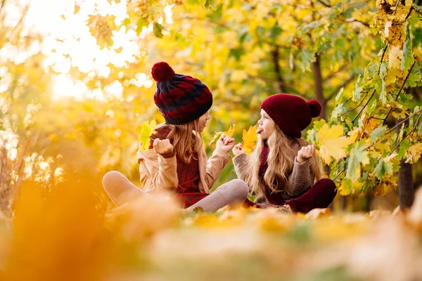 Dziewczyny w kapeluszu siedzieć jesienią Park z liściem klonu i grać, baw się dobrze. — Zdjęcie stockowe
