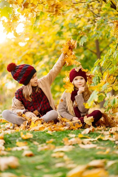 Ragazze in cappello sedersi in autunno Parco con foglia d'acero e giocare, divertirsi. — Foto Stock