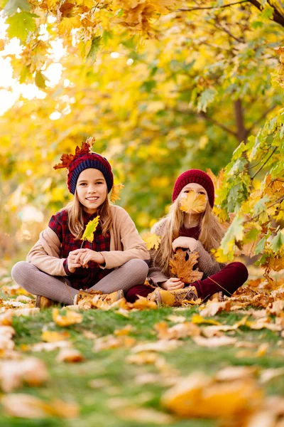 Girls in the hat sit in autumn Park with maple leaf  and play, have fun. — Stock Photo, Image