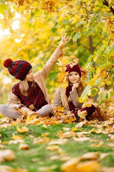 Şapkalı kızlar sonbahar parkında akçaağaç yaprağıyla oturur ve oynarlar. İyi eğlenceler.. — Stok fotoğraf