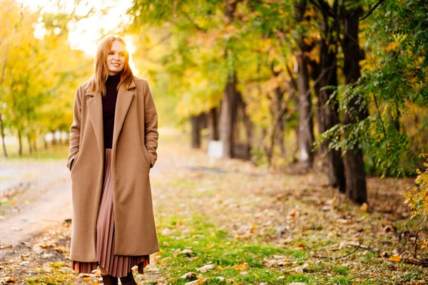 Sonnenuntergang. Ruhige Frau im Mantel steht auf Fußweg im Herbstpark. — Stockfoto