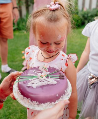 Çimlerde doğum günü pastası yiyen yüzü boyalı bir kız..