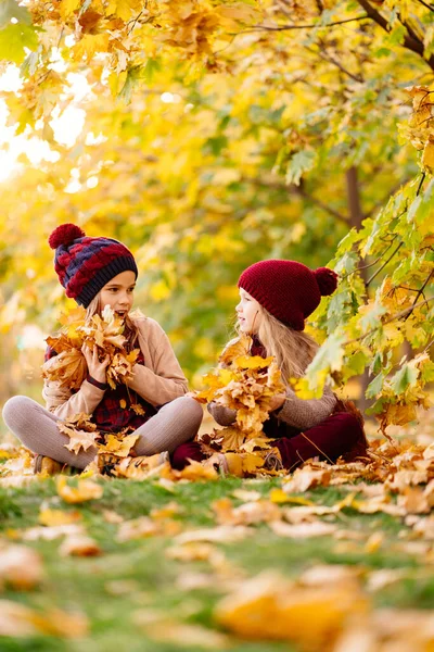 Mädchen mit Hut sitzen im Herbst Park mit Ahornblatt und spielen, haben Spaß. — Stockfoto