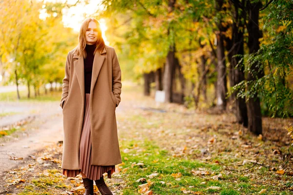 setting sun. calm woman in coat standing on footpath in autumn Park.