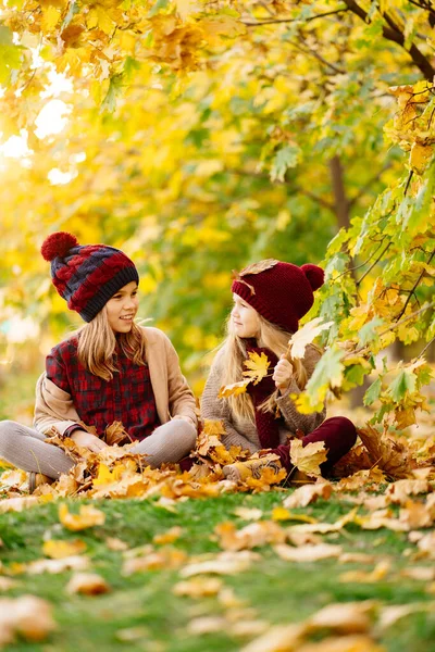 Dziewczyny w kapeluszu siedzieć jesienią Park z liściem klonu i grać, baw się dobrze. — Zdjęcie stockowe
