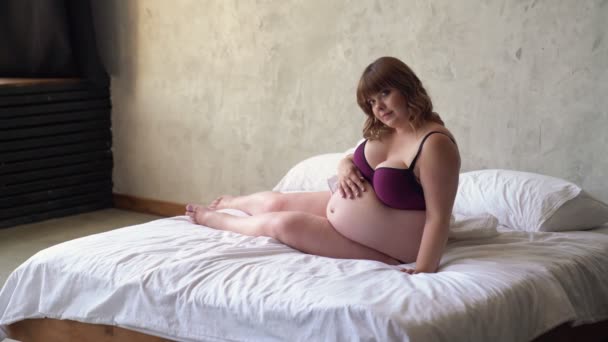 Красивая беременная с избыточным весом в нижнем белье сидит в постели. красота тела. — стоковое видео
