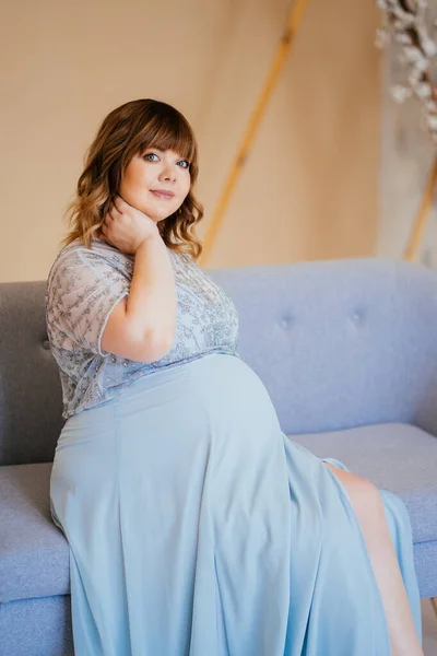 Gravid med övervikt i klänning sittande på soffan — Stockfoto