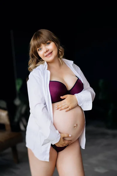 Femme enceinte en surpoids en sous-vêtements debout et caressant le ventre. — Photo