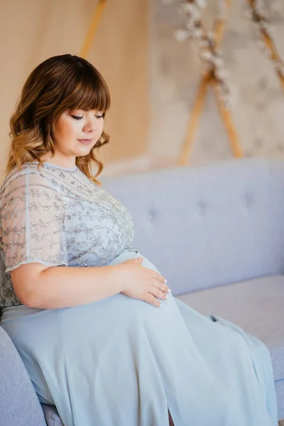 Gravid med övervikt i klänning sittande på soffan — Stockfoto