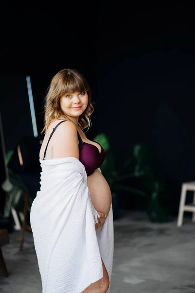 Zwangere vrouw met overgewicht in ondergoed en witte mantel strelen buik. — Stockfoto