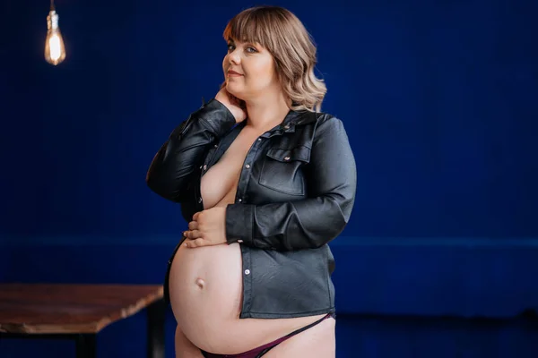 Topless är död. naken gravid kvinna i en skinnskjorta poserar mot en blå vägg. — Stockfoto