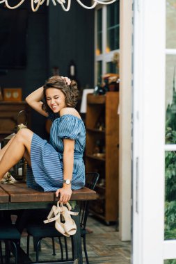 Çıplak ayakla masada oturan ve sandalet tutan bir kız..