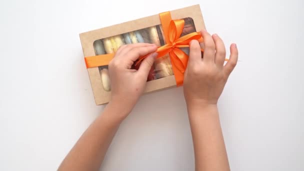 Manos de los niños desatar lazo en la caja con macarrones multicolores — Vídeos de Stock