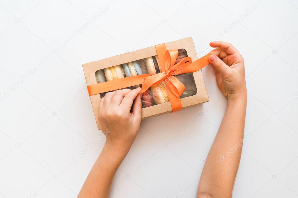 children's hands untie bow on box with multicolored macarons