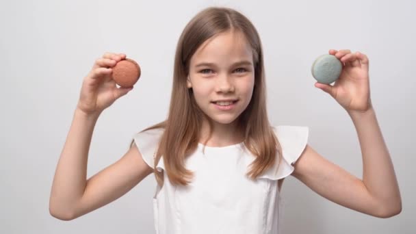 Lány játszik a macaronok, tartja a cookie-kat, mint a szemüveg és dobja a kezét oldalra — Stock videók