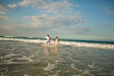 Beyazlı çift sahilde suyun içinde koşuyor..
