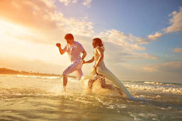 Casal em branco correndo na praia no pôr do sol . — Fotografia de Stock