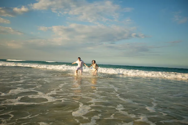 couple in white running forward in water on beach.