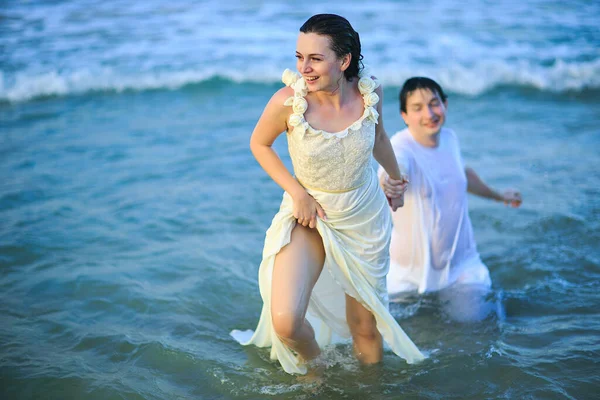 woman leads man by hand in sea water on beach.
