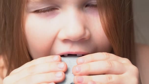 Close-up. menina com caído-out dentes de bebê morde bolo macaron . — Vídeo de Stock