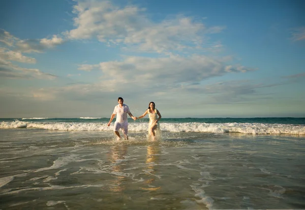 Пара в белом бежит вперед в воде на пляже. — стоковое фото