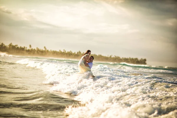 couple in white on sea beach in waves at sunset