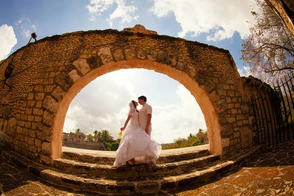 Couple en blanc vêtements de mariage se tiennent à la vieille arche de pierre. voyage de lune de miel. — Photo