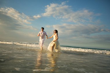 Beyazlı çift sahilde suyun içinde koşuyor..