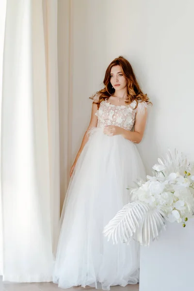 Novia en el vestido de novia se encuentra cerca de la pared blanca — Foto de Stock