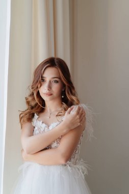 Tüylü gelinlik giymiş, omuzlarını sarıyor.