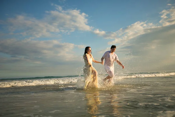 Coppia in bianco correndo in avanti in acqua sulla spiaggia. — Foto Stock