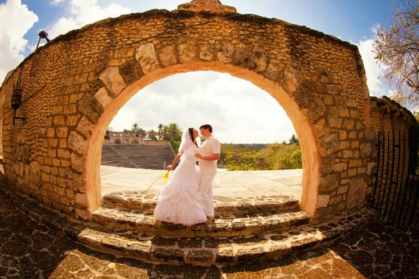 Couple en blanc vêtements de mariage se tiennent à la vieille arche de pierre. voyage de lune de miel. — Photo