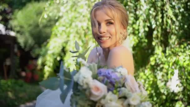 Mariée avec bouquet sur fond d'arbres verts dans le jardin d'été et feuilles. — Video