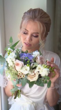 Güzel bir gelin, mavi gözlü ve pencerede oturan bir buket.