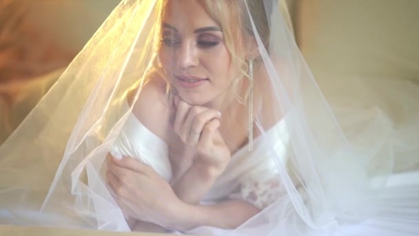 Krásná nevěsta pod závojem a v hedvábném županu ležícím na posteli. — Stock video