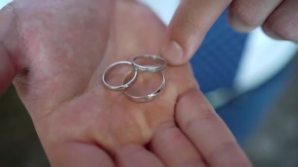 Drie trouwringen, hun vinger corrigeren aan de hand van een man. close-up. — Stockvideo