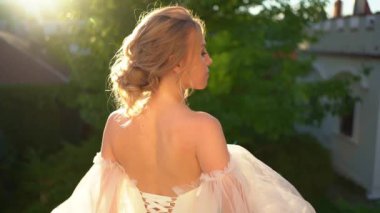 Çıplak omuzlu gelin gün batımında ayakta duruyor.