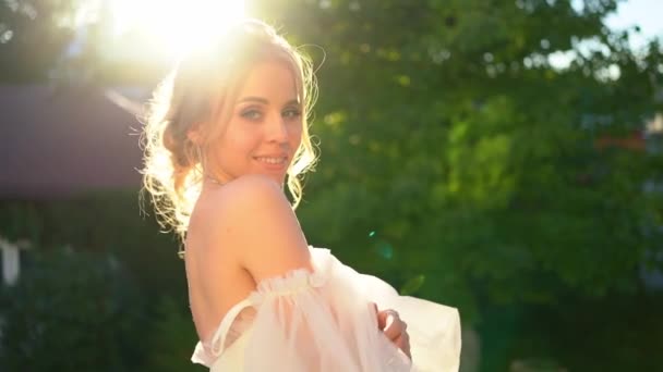 Beautiful bride in dress with bare shoulders standing in rays of setting sun — Stock Video