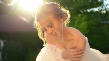 Gelinlik giymiş, omuzları çıplak, gün batımının ışınlarında duruyor.