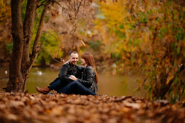 Paar sitzt am Ufer des Flusses im Herbstpark. — Stockfoto