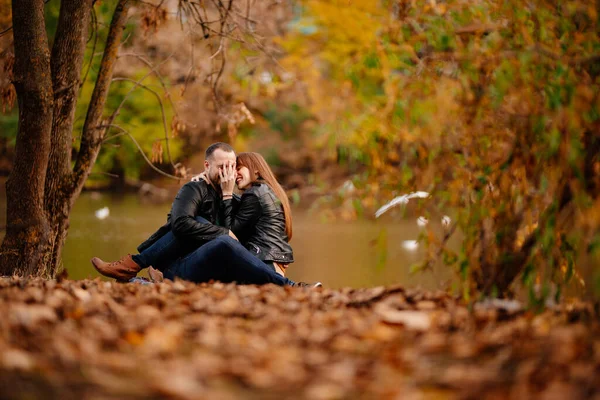 Casal sentado na margem do rio no parque de outono . — Fotografia de Stock