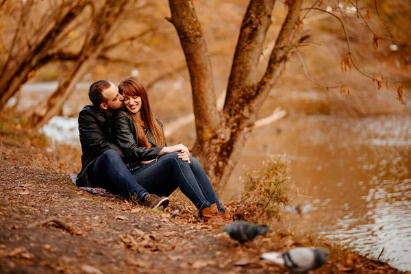 Couple assis sur la rive de la rivière dans le parc d'automne. — Photo