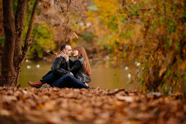 Pár sedí na břehu řeky v podzimním parku. — Stock fotografie