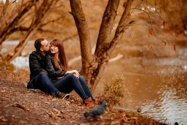 Sonbahar parkında nehir kıyısında oturan çift.