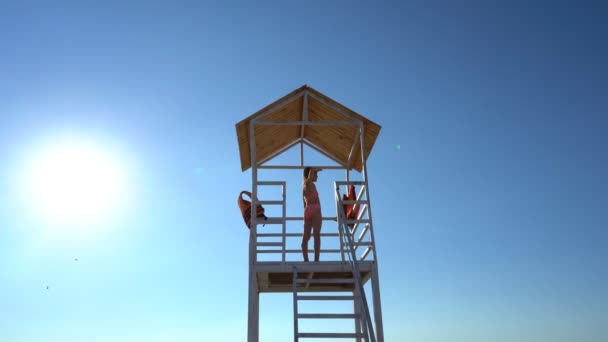 Tonårstjej står på badvakt torn på stranden mot molnfri himmel. — Stockvideo