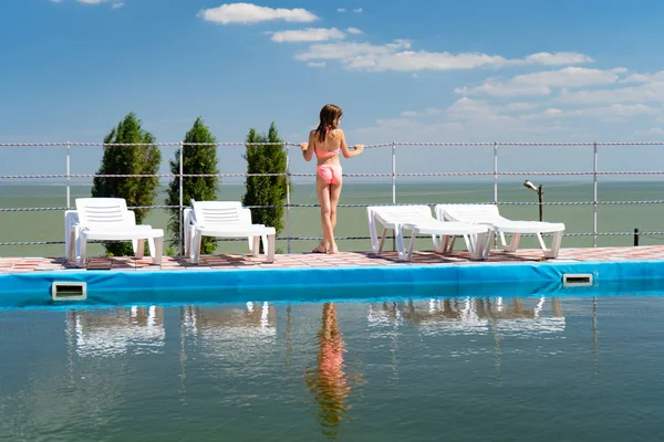 Adolescente chica en traje de baño se encuentra entre tumbonas por el fondo de la piscina mar —  Fotos de Stock