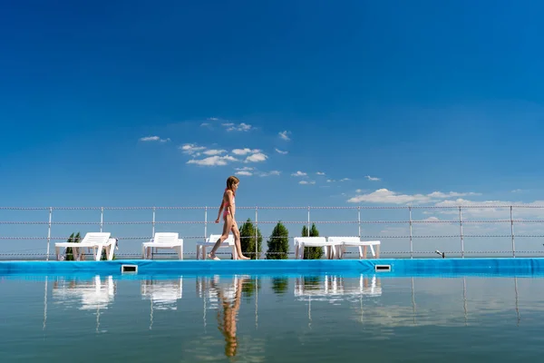 Adolescente chica en traje de baño va a lo largo de piscina fondo cielo —  Fotos de Stock